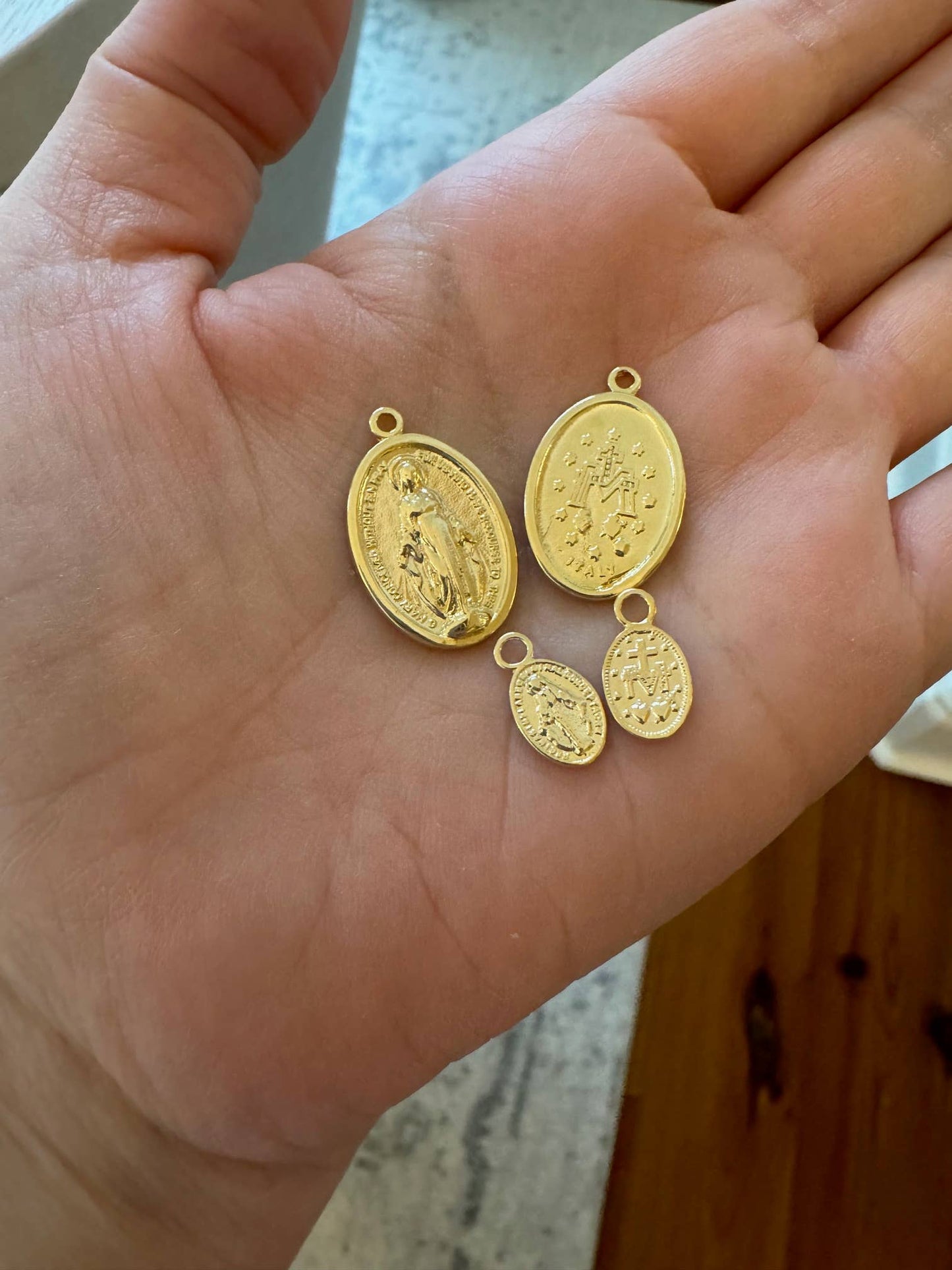 Four gold religious pendants on a person's hand with a blurred background.