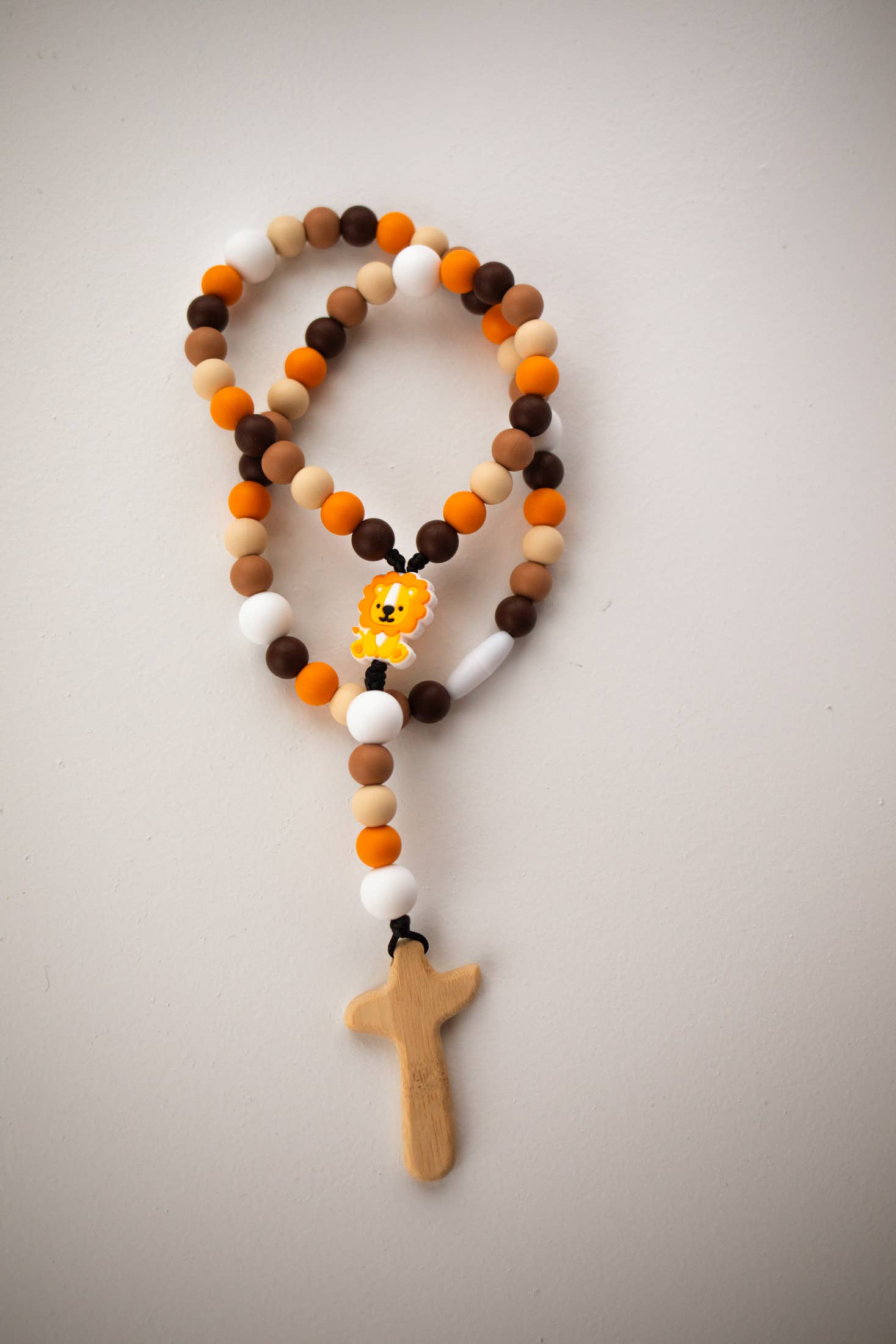 Rosary with multicolored beads and a wooden cross on a light gray background