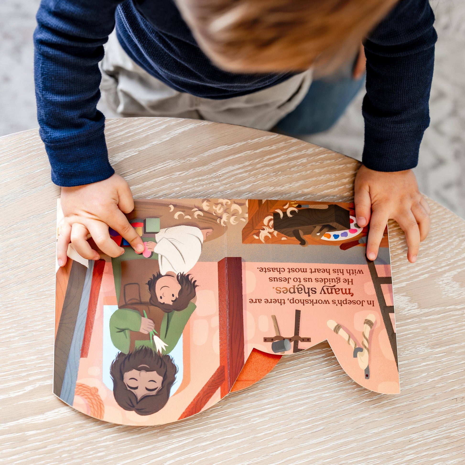 Child playing with a colorful book on a wooden table