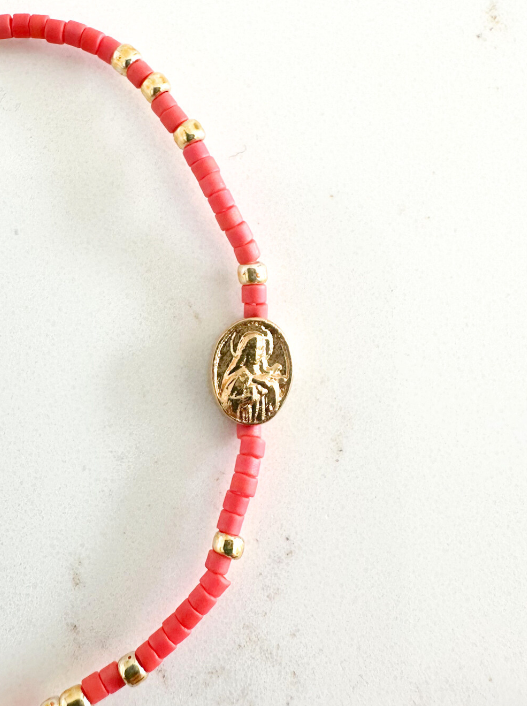 Bracelet with red beads and a gold charm on a light background