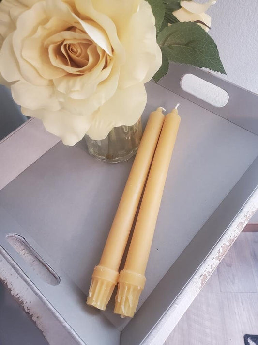 Two beeswax candles and a vase with white roses on a metal tray.