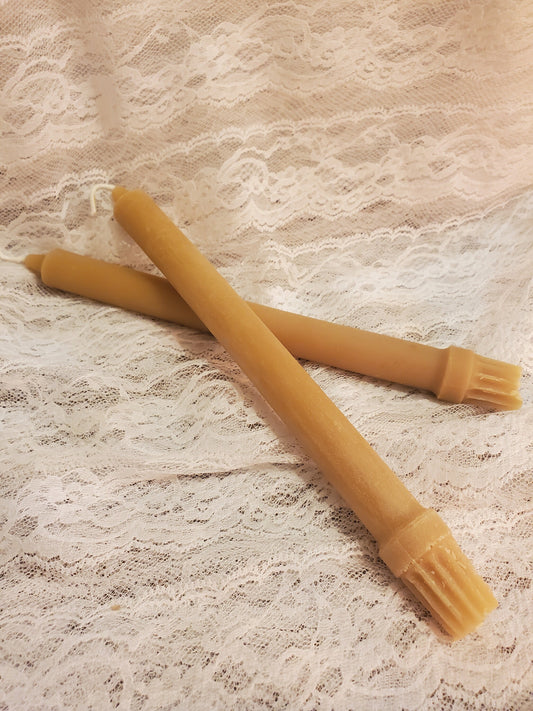 Two yellow beeswax pillar candles on a textured beige surface